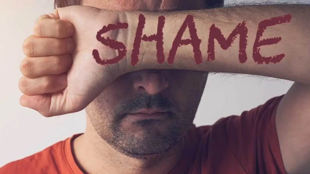 Man hiding shame of porn addiction by covering his eyes with his arm that has the word shame written across it, representing how internalized shame drives porn addiction.
